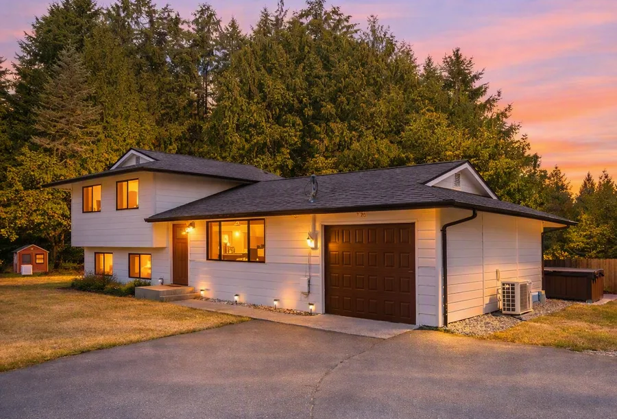 Twilight exterior photo of a home at dusk — warm lights glowing through windows against a pink and orange sunset sky